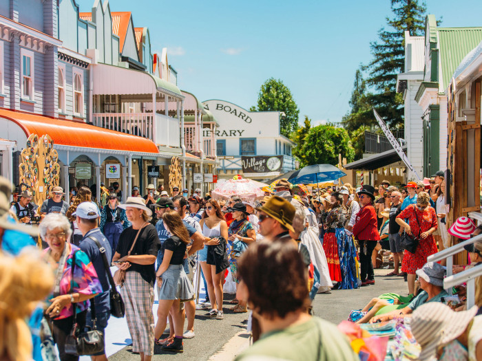 Crowded level asphalt street with historic timber buildings. Paved footpaths under wooden verandas lead to shop entrances. White handrails line a small set of steps on the right.
