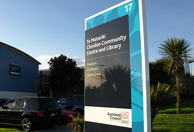 Large sign for Te Matariki Clendon Community Centre and Library in a level asphalt car park. Sign lists Stadium, Childcare and Youth Zone. Auckland Council logo visible at the base.