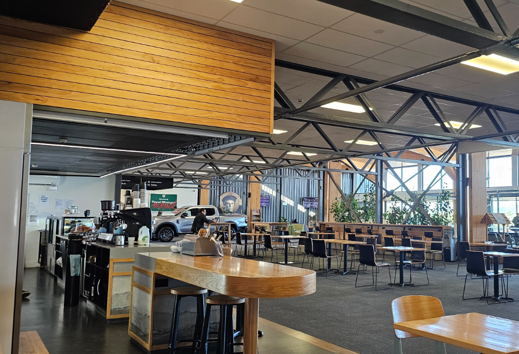 Level floor with grey carpet and dark hard surfaces. Wide clear pathways between standard-height tables and black chairs. High wooden counter with stools. Bright artificial and natural light.