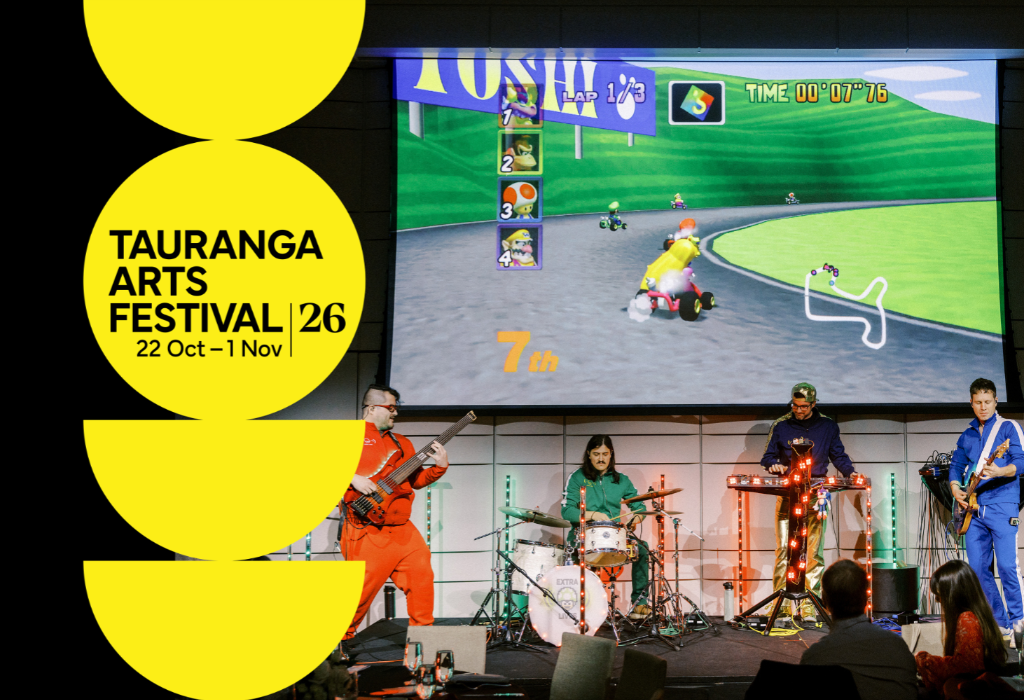 Level, dark carpeted floor area with seating at tables. Musicians perform on a low stage before a large screen. Yellow festival signage with dates is positioned on the left.