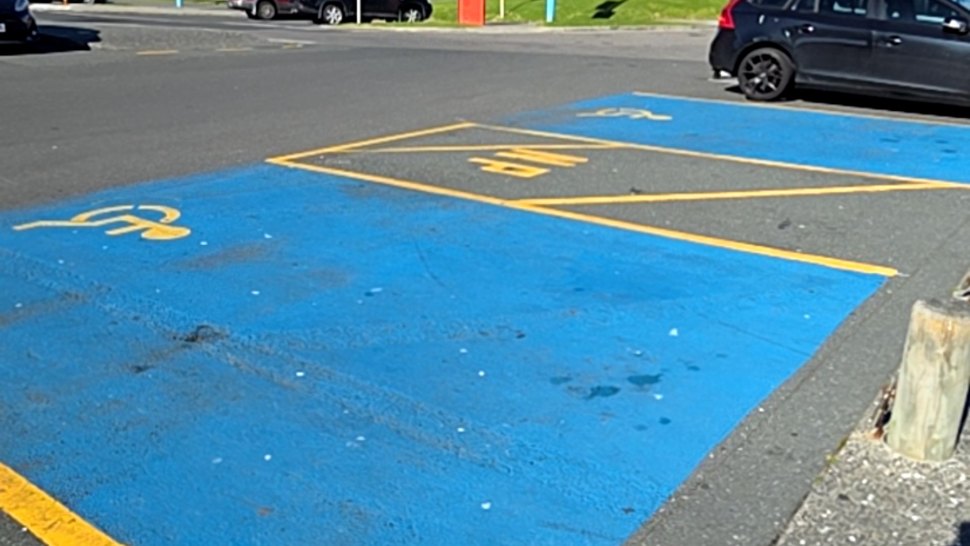 Two accessible parking spaces with blue ground paint, yellow wheelchair symbols, and yellow boundary lines on level asphalt. A yellow "MP" marking sits in a shared zone between the spaces.