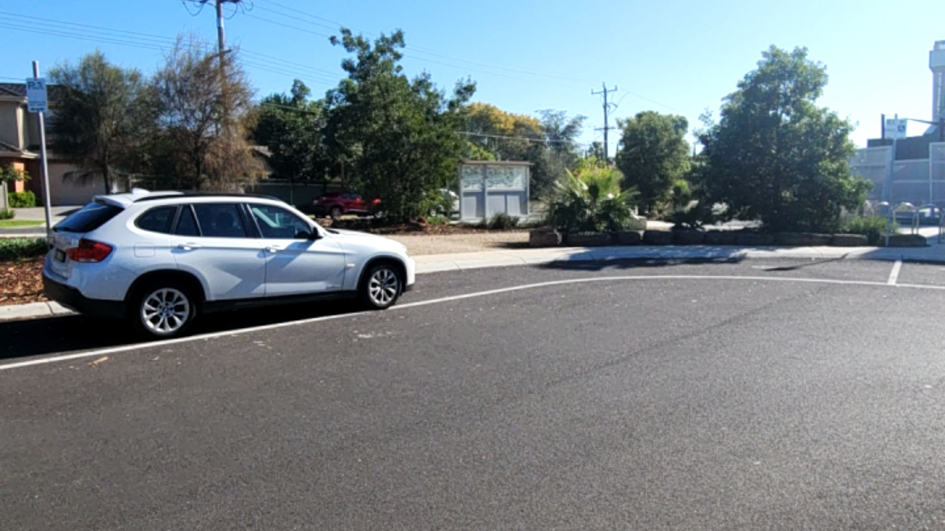 White SUV parked in an accessible bay on level asphalt. A blue sign with a wheelchair symbol marks the space, bordered by a concrete kerb and flat pavement.