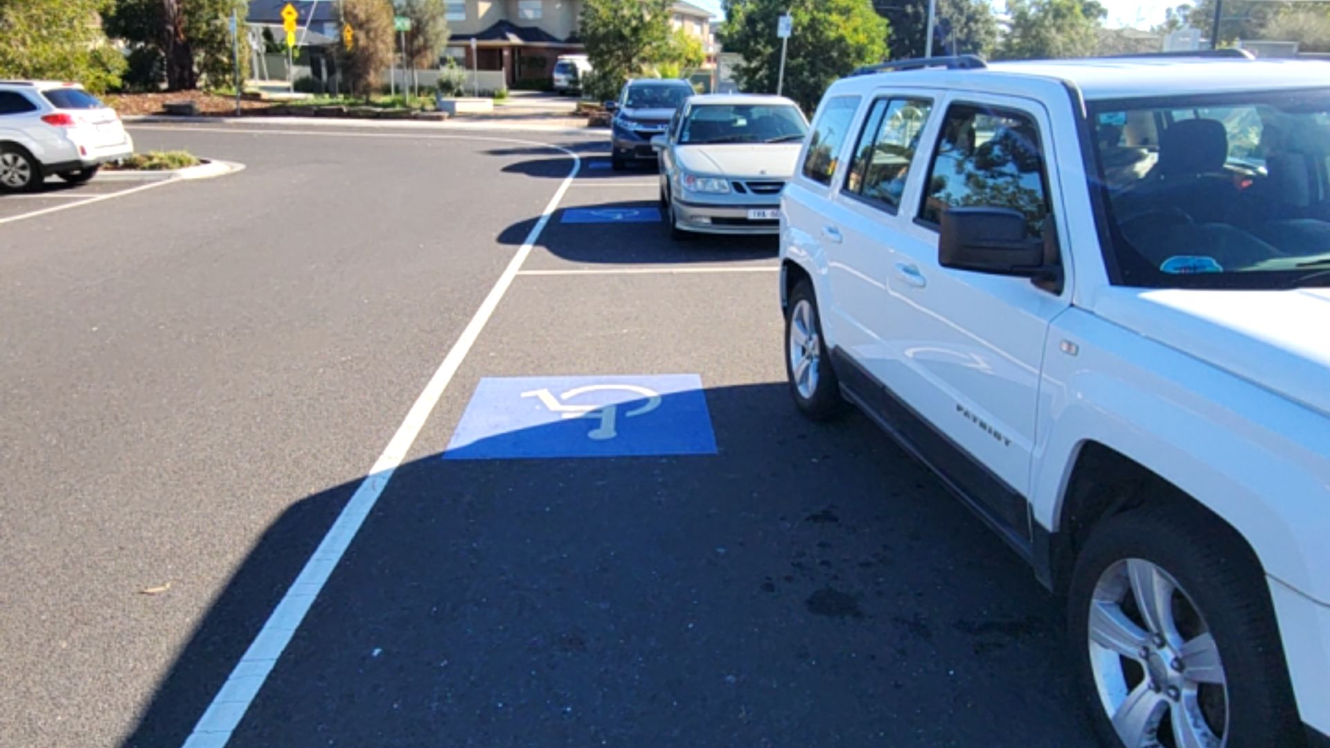 Two accessible parking spaces marked with bright blue and white wheelchair symbols on level asphalt. A white SUV is parked parallel to the spaces.