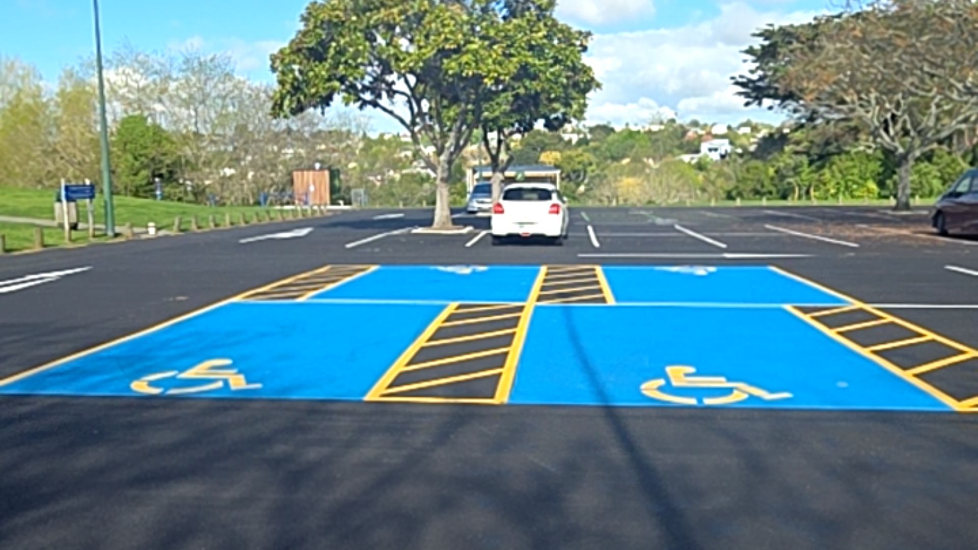 Two level, bright blue accessible parking spaces on black asphalt. Yellow wheelchair symbols and diagonal hatch markings define the spaces and shared access zones.