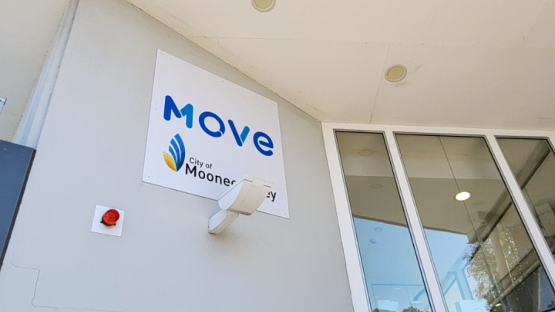 White signage on a grey wall with blue 'MOVE' text and logo. Adjacent large glass-paned entrance with white frames and recessed overhead lighting.