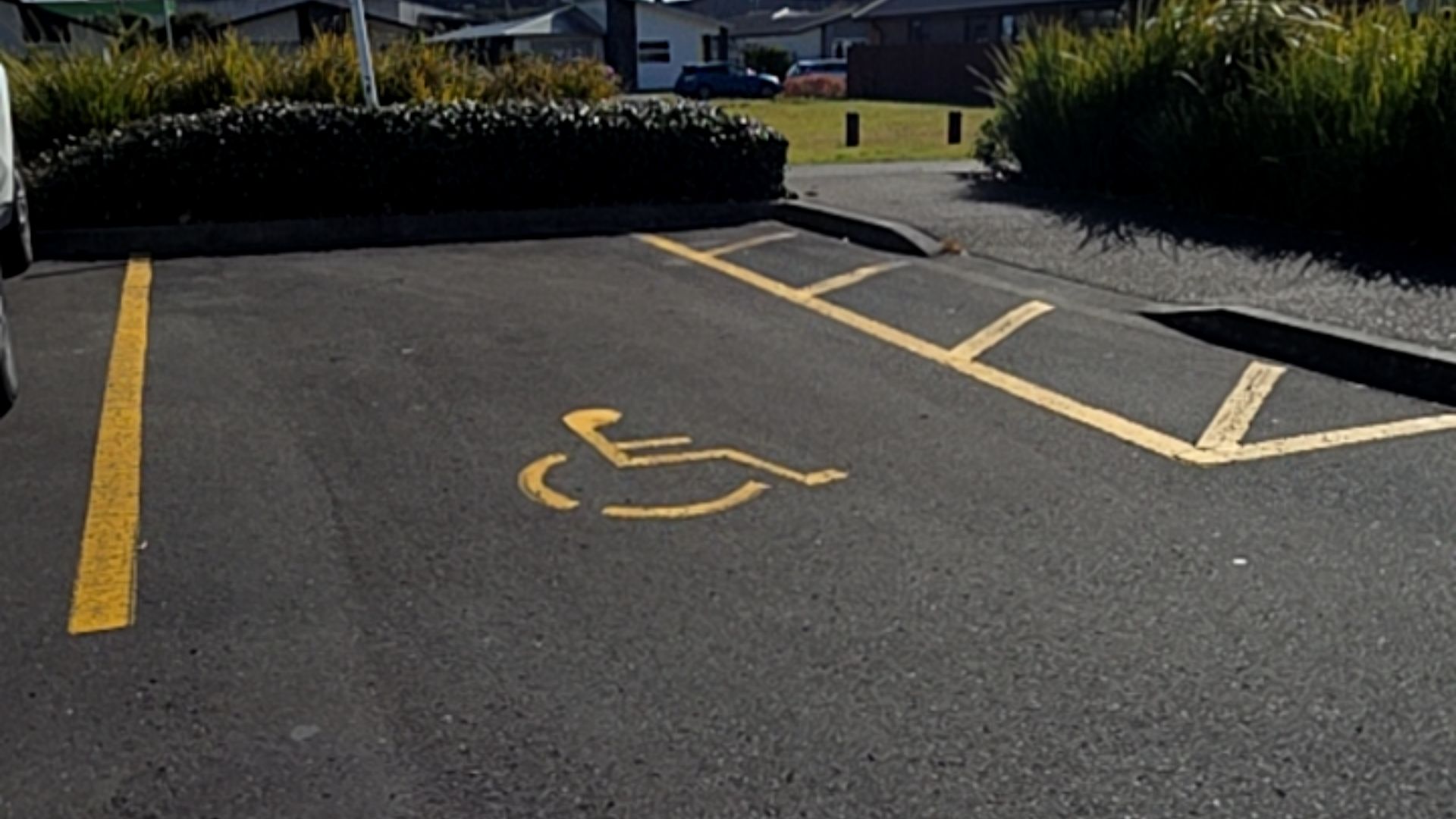 Accessible bitumen parking space with yellow wheelchair symbol and hatched access zone on the right. Level asphalt surface.