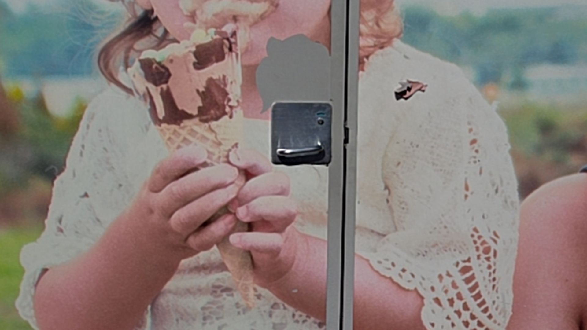 Vertical silver metal frame next to a black rectangular handle with a silver pull lever on a vehicle door. The exterior features a large decal of a child in a white lace dress.