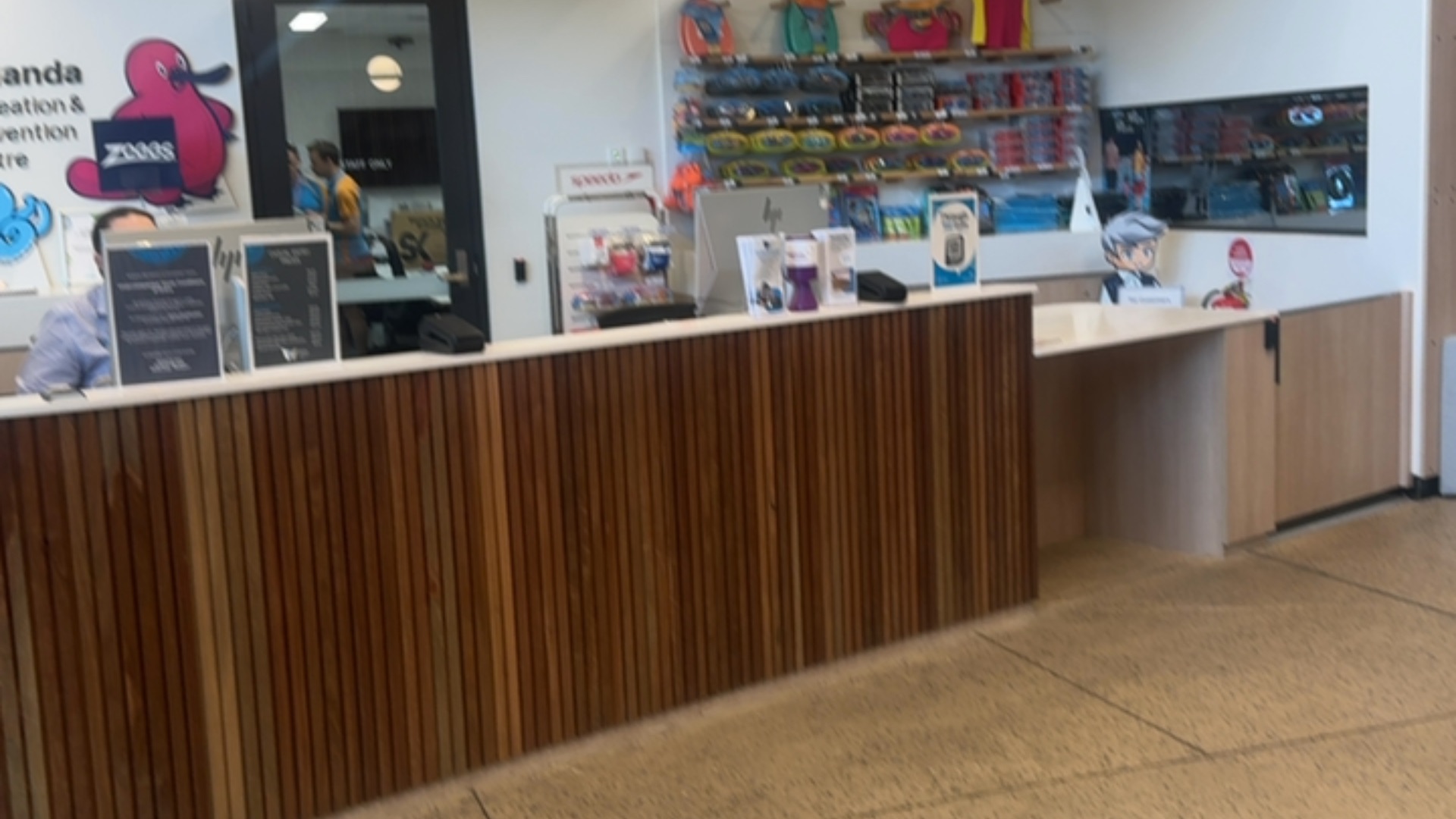 Timber-slatted reception desk with a lowered counter section on the right. Level, polished stone flooring leads to the desk in a brightly lit indoor service area.