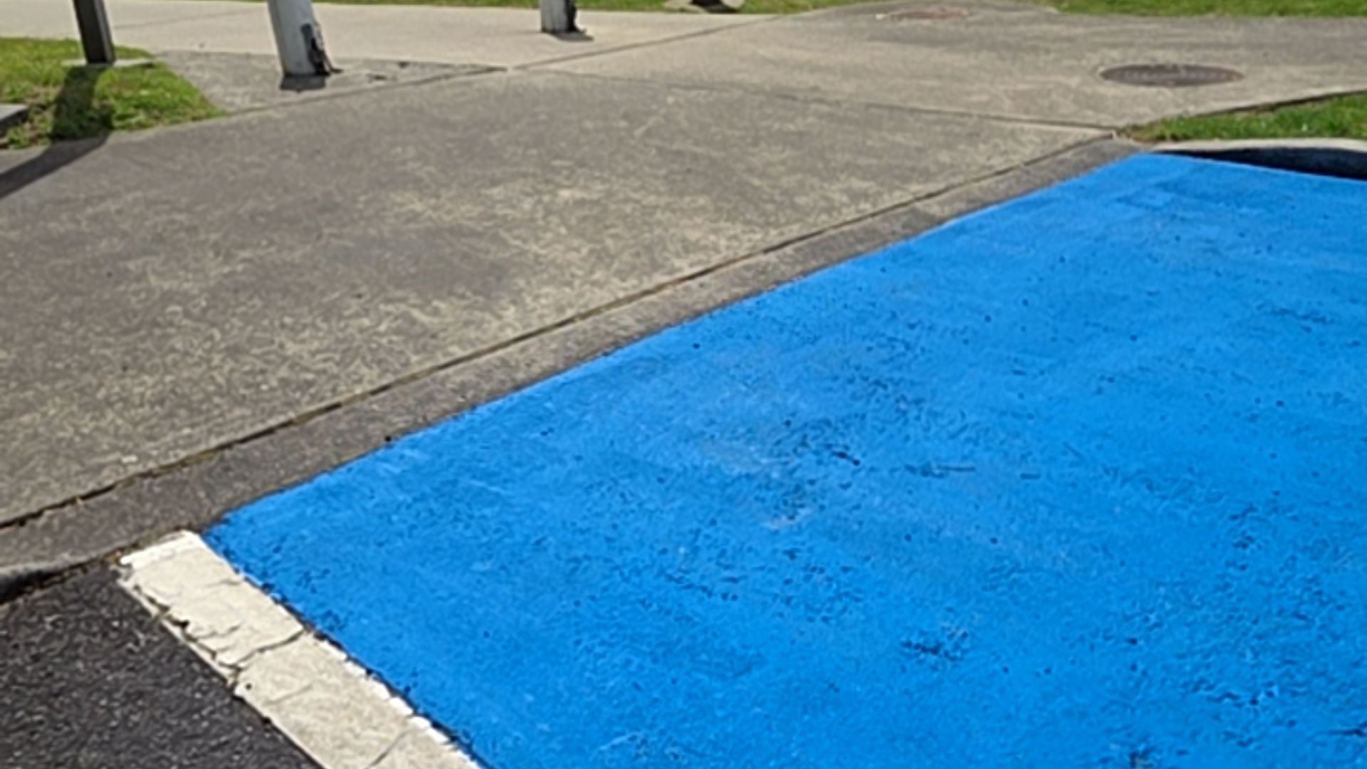 Bright blue painted parking area next to a grey concrete footpath with a level transition. A white painted line borders the blue surface.
