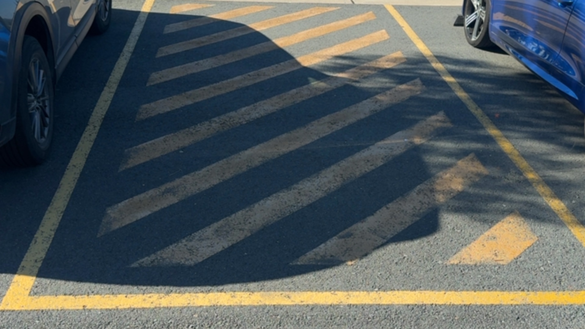 Level asphalt area between two parked cars, marked with yellow diagonal cross-hatching and a yellow rectangular border. The ground surface is flat and unobstructed.