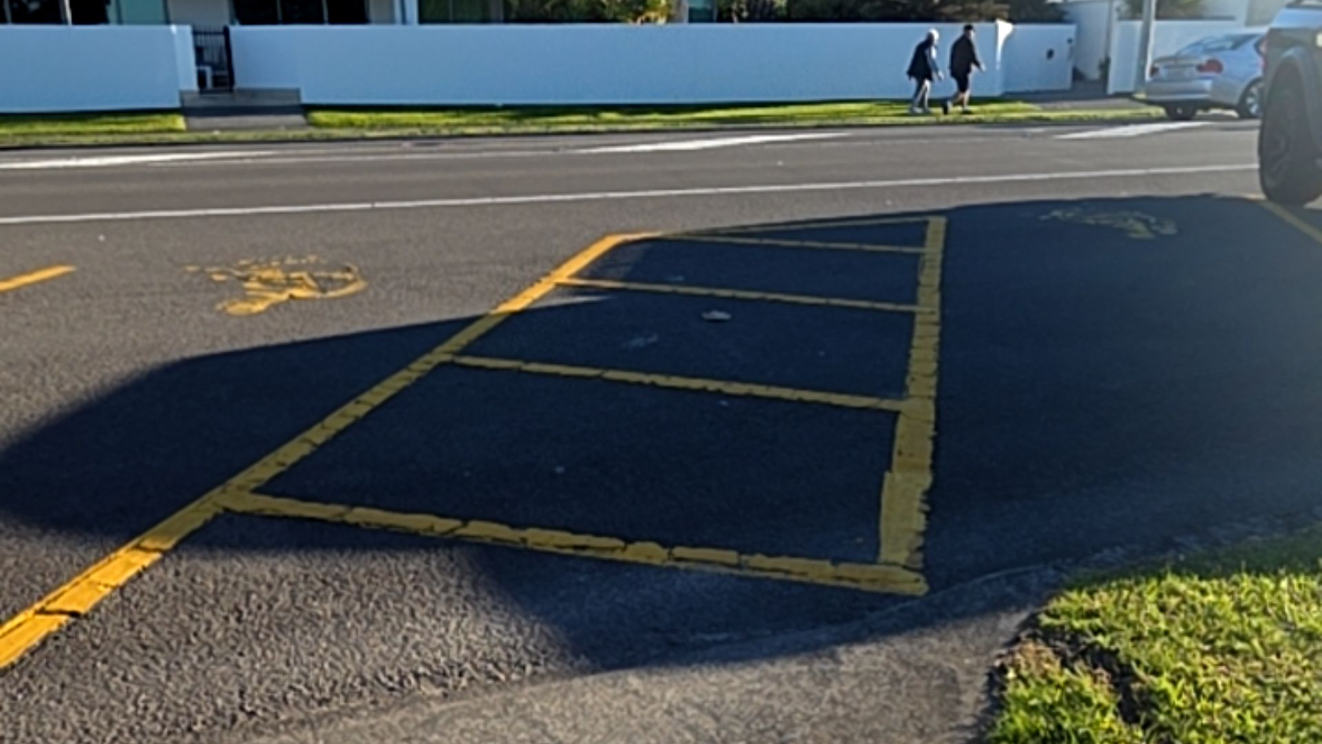 Two yellow wheelchair symbols painted on level asphalt, flanking a yellow-bordered rectangular hatched access zone for parking.