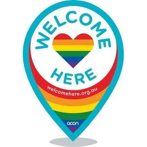 The Wecome Here logo with the words "Welcome" in here, outlining a circle around a heart with a rainbow inside a map pin