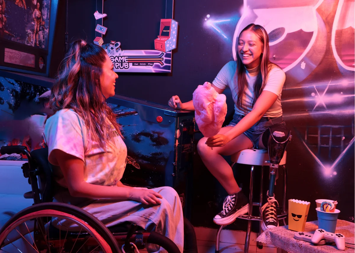 A person with a prostetic leg, sharring cotton candy with a person in a wheelchair in an arcade.