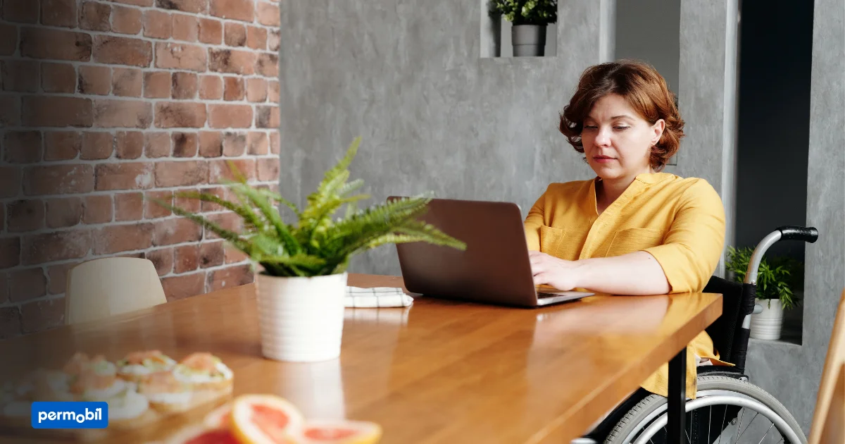 A woman in a wheelchair working on a laptop at a table.