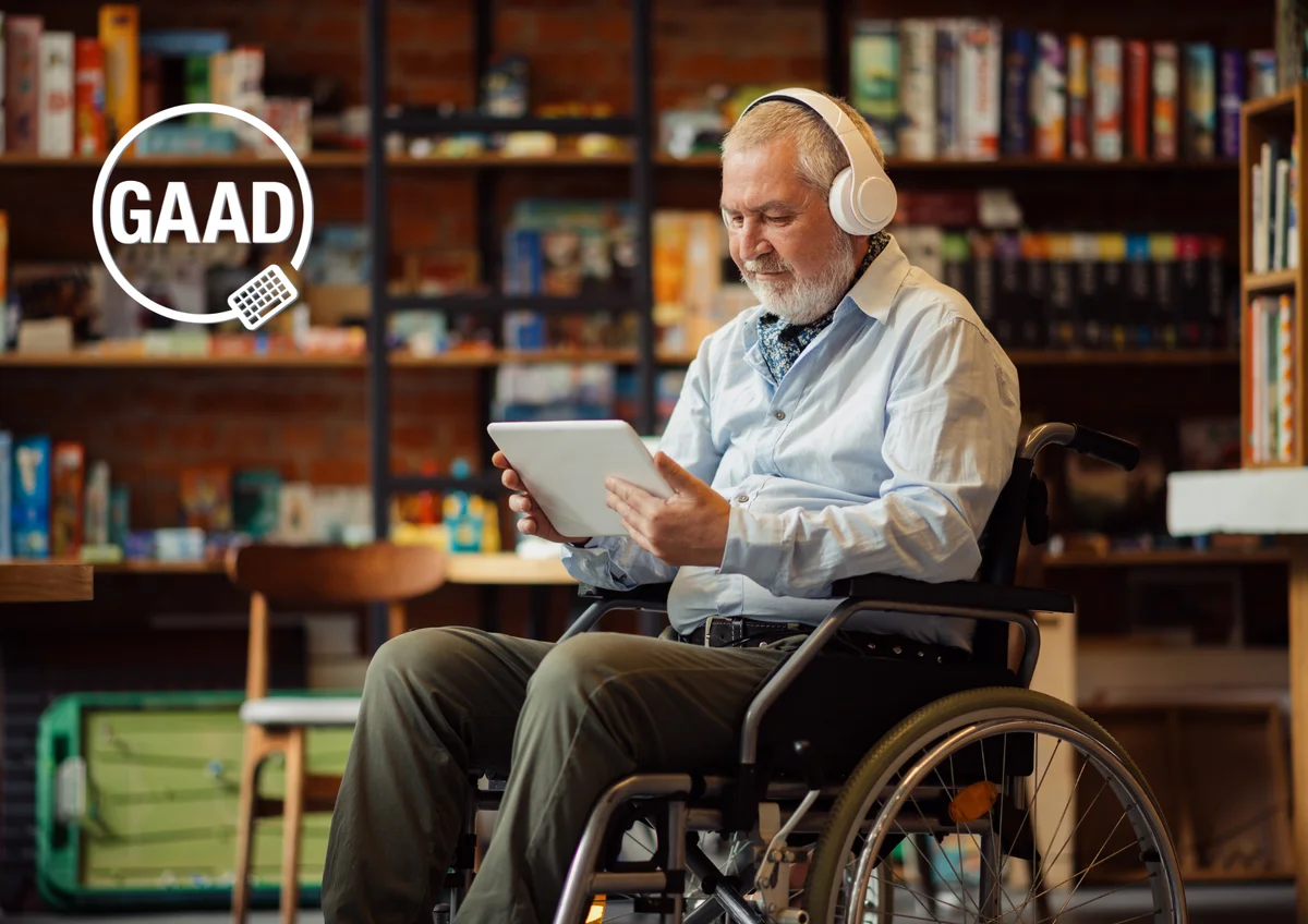 An older white man in a wheelchair, holding a tablet while wearing headphones, engaging with a piece of technology. The GAAD logo displays in the top left corner of the image.