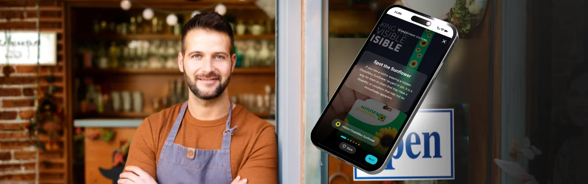 A shop owner standing in front of his store with a Hidden Disabilities Sunflower icon on a phone screen off to its right side