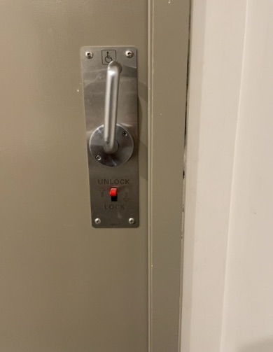 Light grey door with silver lever handle, accessibility symbol, and red toggle switch reading 'UNLOCK' and 'LOCK', set to 'LOCK'.