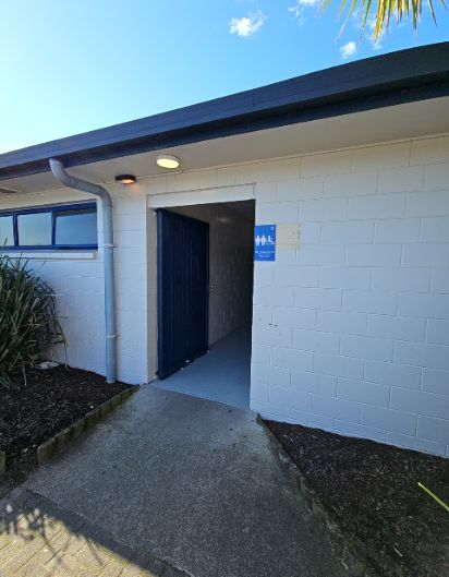 Wide concrete ramp leads to an open doorway with a level grey floor. A blue accessibility sign is on the white brick wall. Two exterior lights are mounted above the entrance.