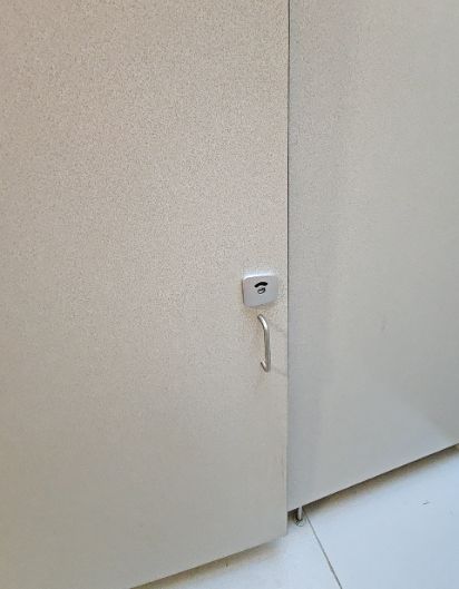 Grey textured locker door with a small silver pull handle and a square electronic lock plate above it, featuring a black contactless access symbol.