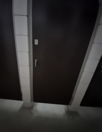 Dark grey walls divided by a light grey block column. A handle and small switch are on the left wall, above a level, light grey floor.