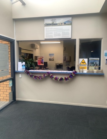 Level entrance to dark grey carpeted reception area. Standard height counter with glass screen, no lowered section visible. Well lit.
