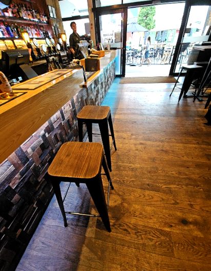 Level timber flooring leads to a wide open doorway. High bar counter with two wooden-topped stools and a clear pathway through to an outdoor seating area with a level threshold.