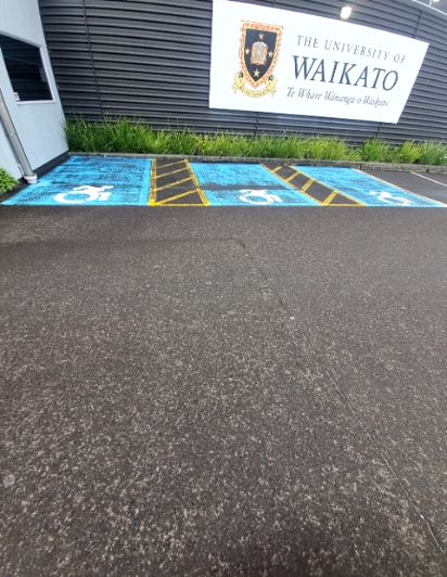 Accessible parking bays, blue with white wheelchair symbols and yellow hatched access aisles, are in front of The University of Waikato sign.