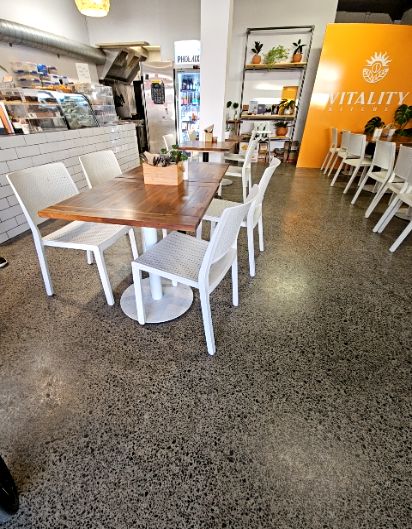 Level polished aggregate concrete floor with wide pathways between wooden tables and white chairs. Well-lit open interior with no visible steps or floor level changes.