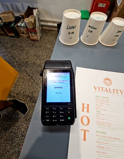 Level, grey speckled floor surface in front of a counter featuring an EFTPOS terminal, drink size indicator cups, and a menu.